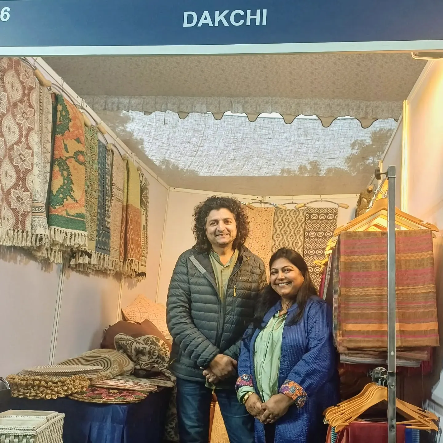 Two women smiling inside the Dakchi stall, with rugs hanging on the walls behind them