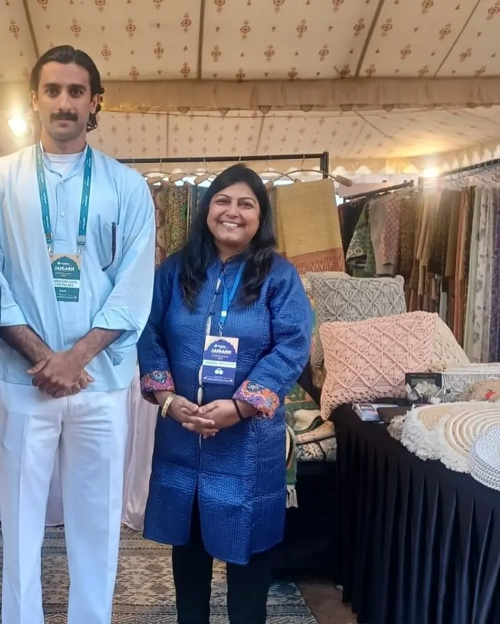 Two visitors wearing event lanyards standing in front of textiles at a Dakchi stall