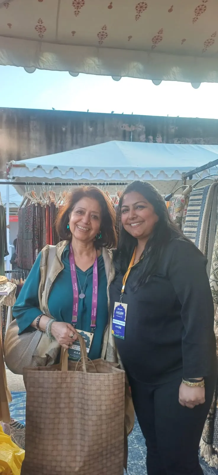 Two women standing in front of a market stall under a tent canopy