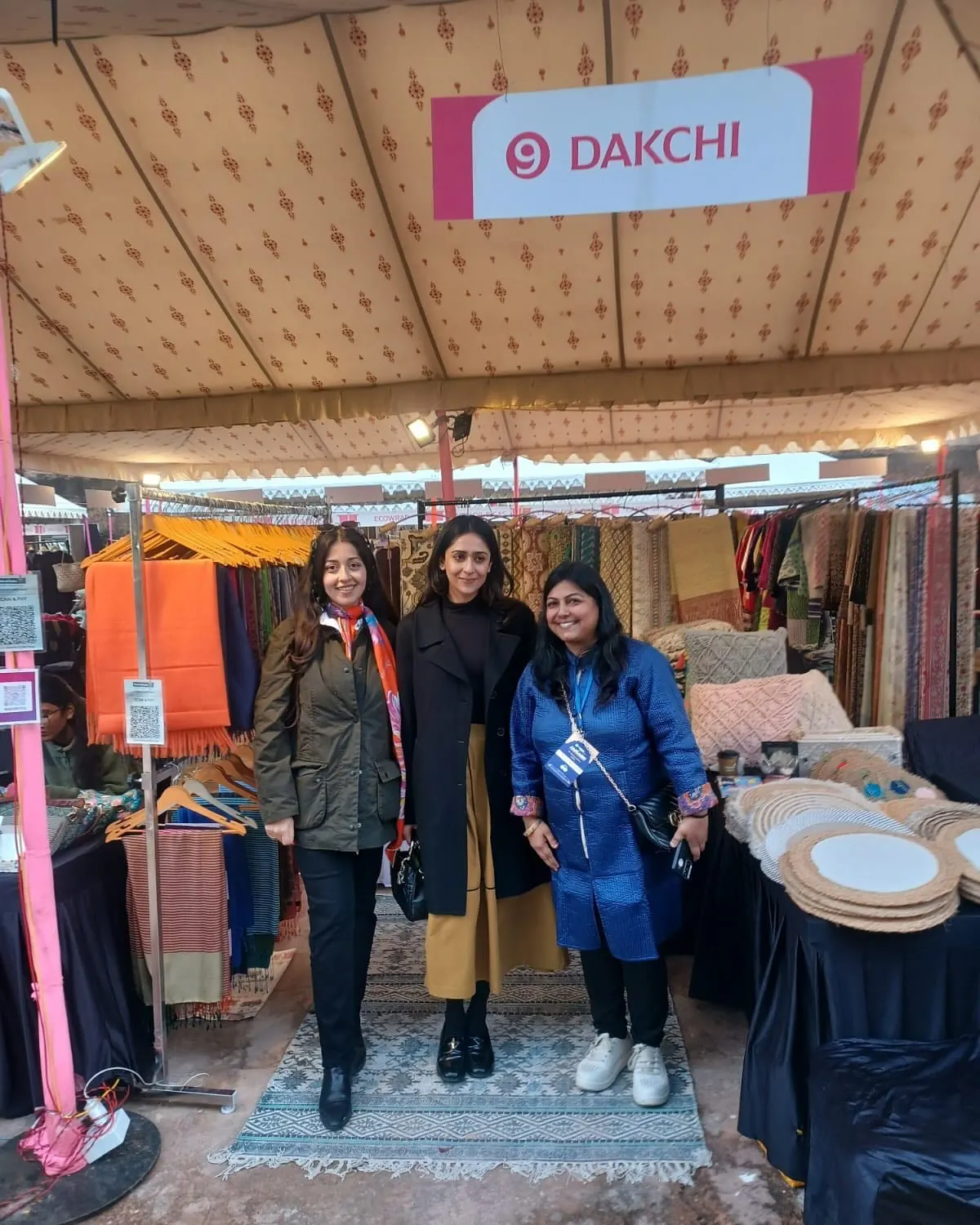 Three women and a child at the Dakchi stall, with rugs on the floor and textiles on rails