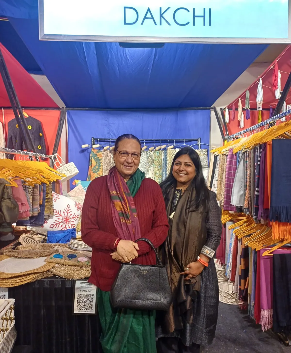 Two women at the Dakchi stall surrounded by colourful textiles